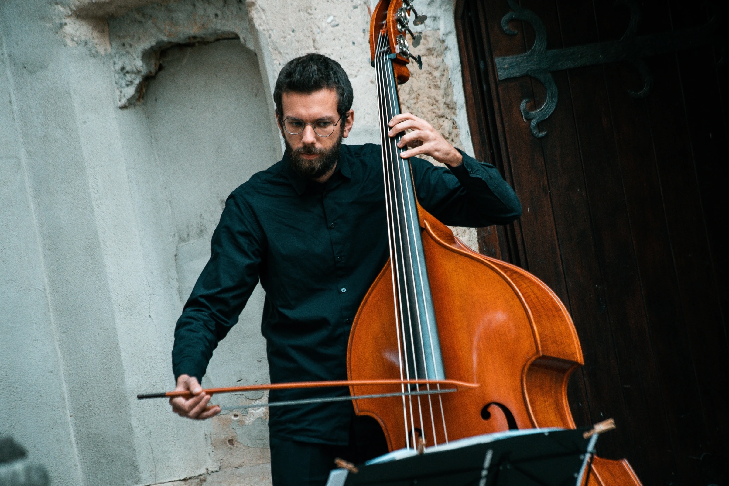 Im Hintergrund des einen Gebäudes spielt ein Mann Cello (Thomas Kolarczyk). Er trägt dunkle Kleidung.